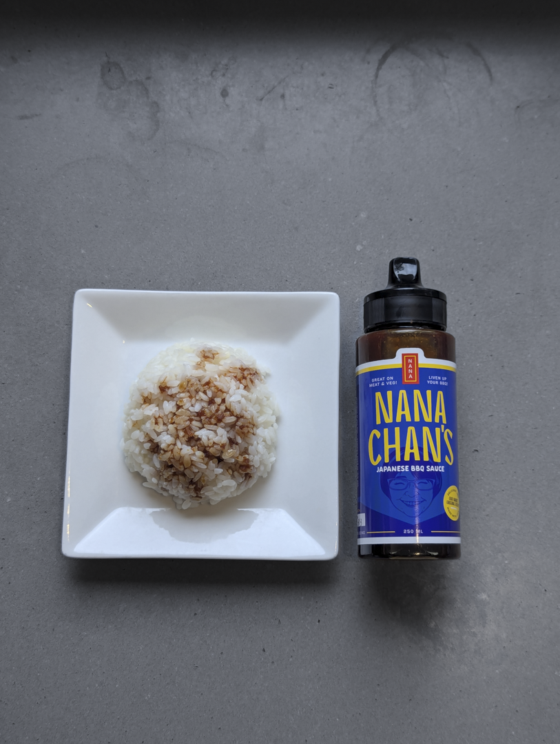 Bowl of rice with a side of Nana-Chan's Japanese BBQ Sauce on a gray surface